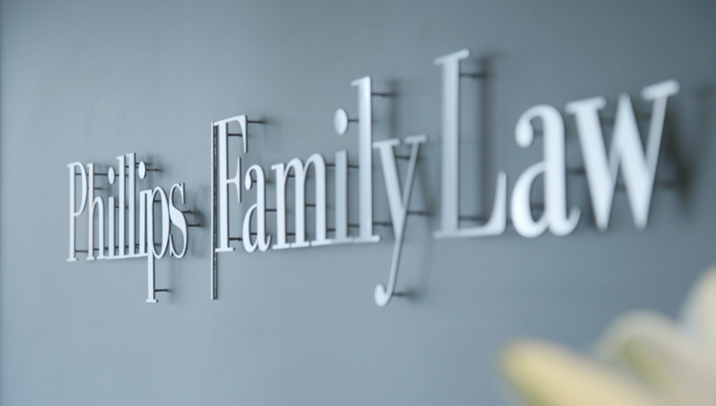 The steel Phillips Family Law sign attached to a grew wall. The individual letters are slightly in front of the wall, creating shadows on the wall of each letter.